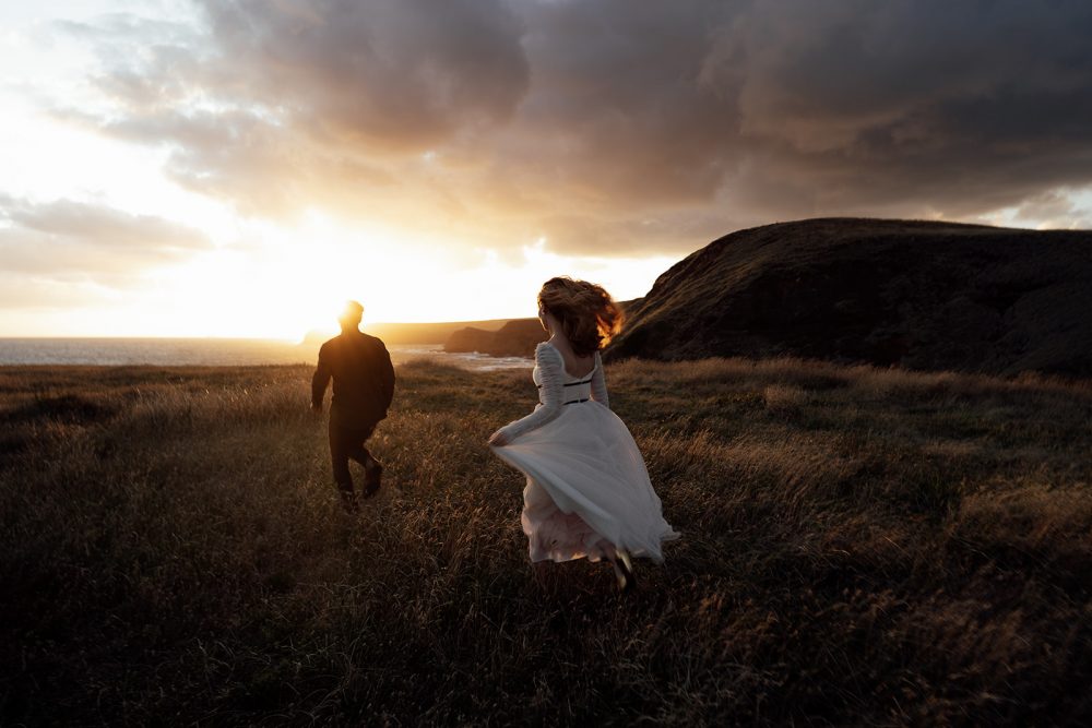 Wedding couple running in the field during sunset