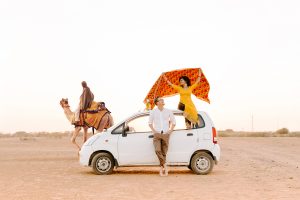 Man and woman leaning on a white car in the desert.